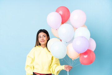 Fototapeta na wymiar Woman holding balloons in a party over isolated blue background standing and looking to the side