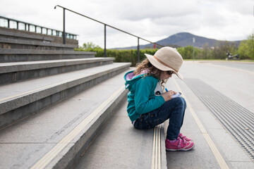 Young girl child seated on the steps outside a library learning reading concentrating