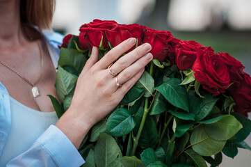 Fototapeta na wymiar guy holds the girl's hand with a wedding ring over a bouquet of red roses