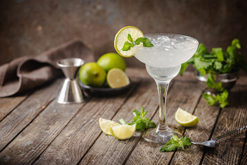Cocktail margarita garnished with lime and mint on wooden background