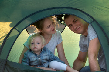 Naklejka premium Happy young family with child in tourist tent at the campsite. Vacation with children