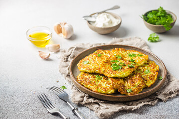 Green zucchini fritters, vegetarian zucchini pancakes with fresh herbs and garlic, served with cream sauce on white background, selective focus