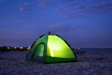 Green tent glows from the inside at night. Camping on the beach.