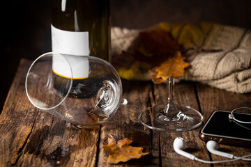 Broken wine glass with bottle, headphones and autumn leaves on wooden table, concept of autumn...