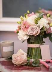 Florist equipment with flowers on white-pink table, top view. Bouquet, candle, secateur, business card of florist shop.
