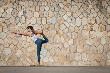 Strong Yoga teacher woman doing an intensive workout along the beach against a seamless pattern wall. Young and attractive woman doing Yoga and Pilates exercises outdoor during a fresh summer day