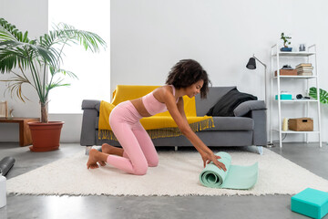 Fototapeta premium Afro woman unrolling her yoga mat at home
