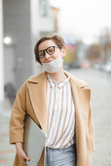 Young attractive girl in medical mask on face with laptop walking  in the city