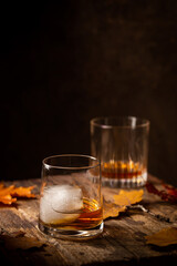 Glass of scotch whiskey and ice on wooden background with autumn leaves