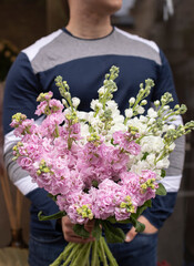 Young man holding delicate flower bouquet of white and purple Delphinium. Bouquet of fresh beautiful flowers. Mother`s day.