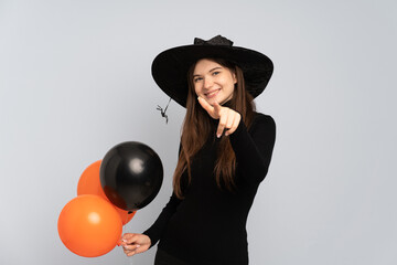 Young witch holding black and orange air balloons pointing front with happy expression