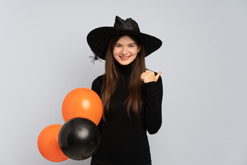 Young witch holding black and orange air balloons giving a thumbs up gesture