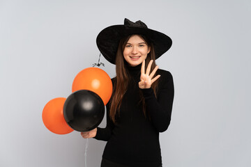 Young witch holding black and orange air balloons happy and counting four with fingers