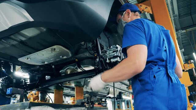 Automobile factory, car production, auto production line. Factory worker is assembling a wheel arch