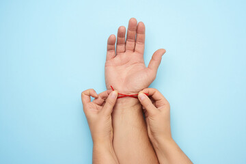 two female hands tie a red woolen thread on the wrist of a male hand