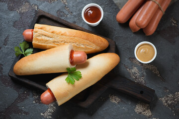 Black wooden serving tray with french or czech style hot-dogs, flatlay over brown stone background,...
