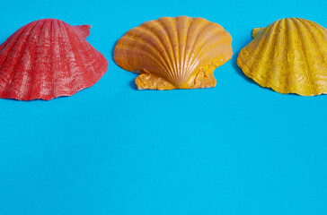 Marine layout. Three sea shells painted in red, yellow and orange on a blue background.