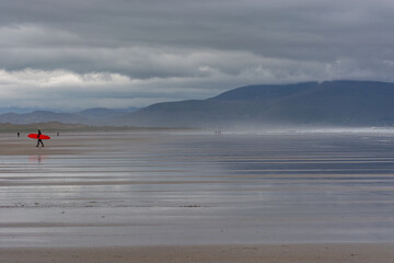Surfer with red surfboard walks across Inch Beach in Ireland.