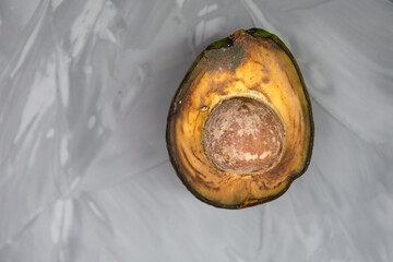 Spoiled avocado with green mold and black spots of rot and fungus on a gray background. Cut natural fruit, half with a round bone. Space for text