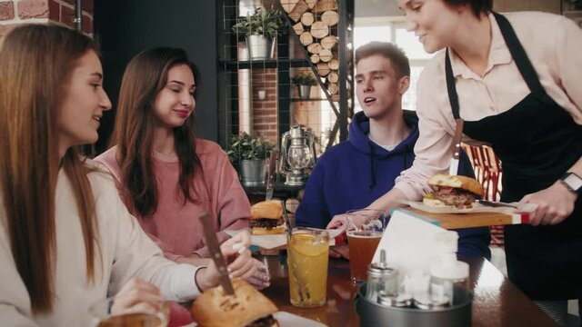 Friends сolleagues sitting in cafe or restaurant have a fun talking as waiter serves meals.