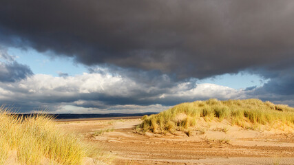 Fototapeta na wymiar Dark rain clouds over Whiteford Bay with sand dunes on the Gower coast - weather and nature concept in a panoramic format - UK