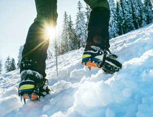 Close up shot of mountain boots with crampons and snow gaiters with backlight sun beams and snowy...