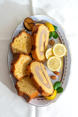 Bizcocho de limón y brazo gitano relleno de crema de café y vainilla con rodajas de limón servido en bandeja de lujo con decoración de frutos secos y hojas verdes en vertical.