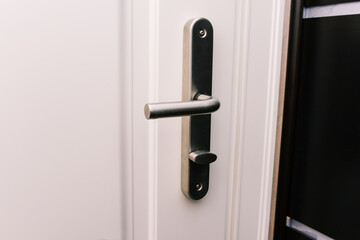 White door and handle. Modern chrome handle in your hotel room or home. Entrance to an apartment, office, or bedroom. Detail of a wooden door. Interior of a house or hotel