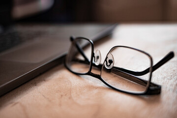 Background image of business office with laptop on wooden desk, focus on black hard rim glasses in foreground, copy space. Out of focus. Blurred