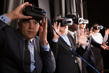 Portrait of scared businessman taking off virtual reality glasses on background of his coworkers. Concept of mixing illusion and reality in business..