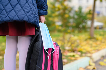 Medical mask and schoolbag in the hand of a schoolgirl. Mask mode for schoolchildren during a...