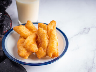 Close-up of deep-fried dough sticks or Chinese doughnut sticks on white plate and a glass of...