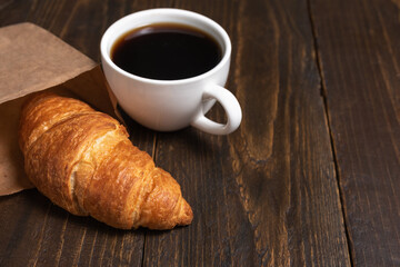 Obraz na płótnie Canvas Cup of coffee and croissant in paper bag