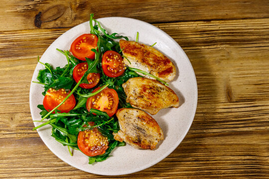 Fried chicken breast with salad of fresh arugula and cherry tomatoes on wooden table. Top view