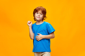 Red-haired boy in a blue t-shirt gestures with his hands smile yellow background.