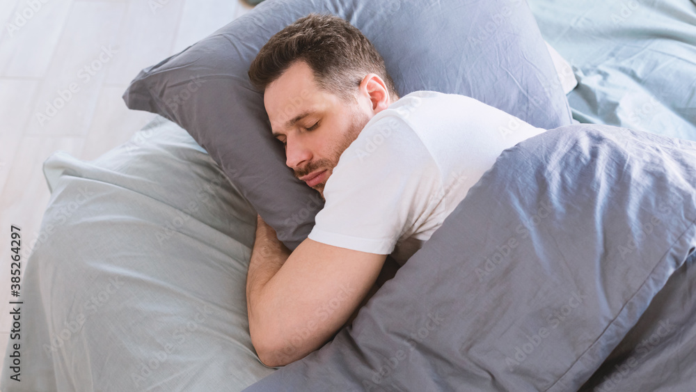 Poster man sleeping hugging pillow lying in bed resting in bedroom