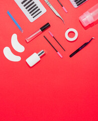 Eyelash extension tools on an orange background, free space for text, top view. Artificial eyelashes, tweezers, microbrushes, patches and brushes for lashmaker.
