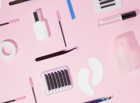 Things for the work of lash-makers, artificial eyelashes, microbrachis, glue, tweezers, combs, brushes for eyelash extensions. Eyelash extension, painting of eyebrows. Top view, pink background.