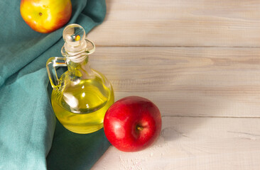 Apple cider vinegar in a glass decanter on a light wooden table. Apples nearby. Free space.