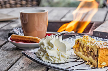 Cafe table with cup of coffee with a biscuit and apple pie with whipped cream, and in the...
