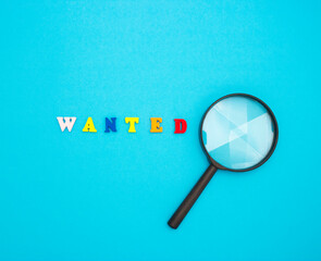 Search for employees to work. The word WANTED in colored wooden letters on a blue background and a magnifying glass.