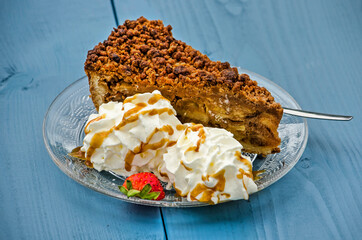 Glass sauces with apple pie and whipped cream with honey and a half strawberry on a light blue wooden table