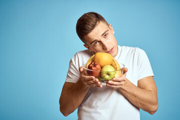 Happy man with fresh fruits gesturing with hands blue background white t-shirt vitamins bananas oranges apples