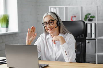 Portrait of smiling grey-haired mature woman using laptop for a online meeting, video call, video conference. Communication online with colleagues or relatives. Online education, remote working.