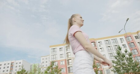 Blond woman playing with a flying disc outdoors in an urban park in a low angle view looking up against a cloudy sky with apartment blocks in the background - Powered by Adobe