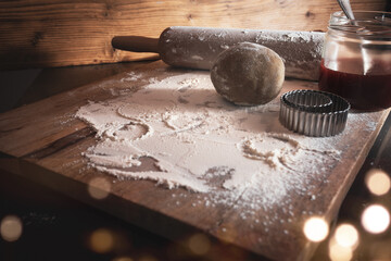 Baking utensils and dough for christmas cookies on wooden cutting board with golden bokeh....