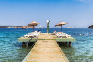 Beach wooden pier with sun umbrellas and beach loungers in Mediterranean sea