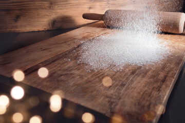 Baking utensils and flour for christmas cookies on wooden cutting board with golden bokeh....