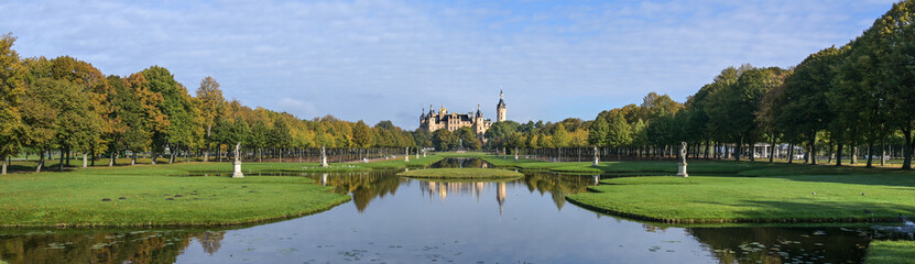 Fototapeta na wymiar Panorama of the Schwerin castle and the park with water canals, lawn and trees, blue sky with copy space, wide panoramic format