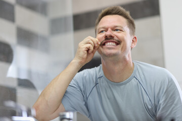 Man smiles and holds his mustache in front of mirror. How to shave your mustache concept
